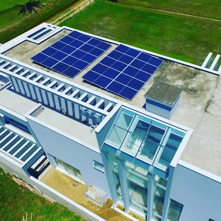 Vista aérea de edificação moderna de linhas retas, com dois conjuntos de módulos fotovoltaicos sobre a laje plana da cobertura