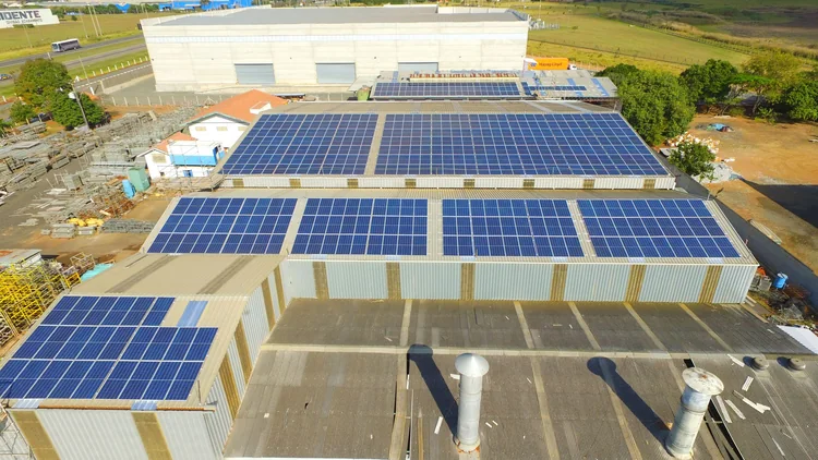Vista aérea de pátio industrial com vários galpões, cada um com módulos fotovoltaicos instalados na cobertura