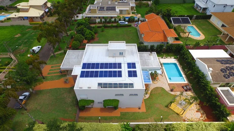 Vista aérea de sobrado moderno em condomínio, com piscina e um conjunto de módulos fotovoltaicos instalado no telhado